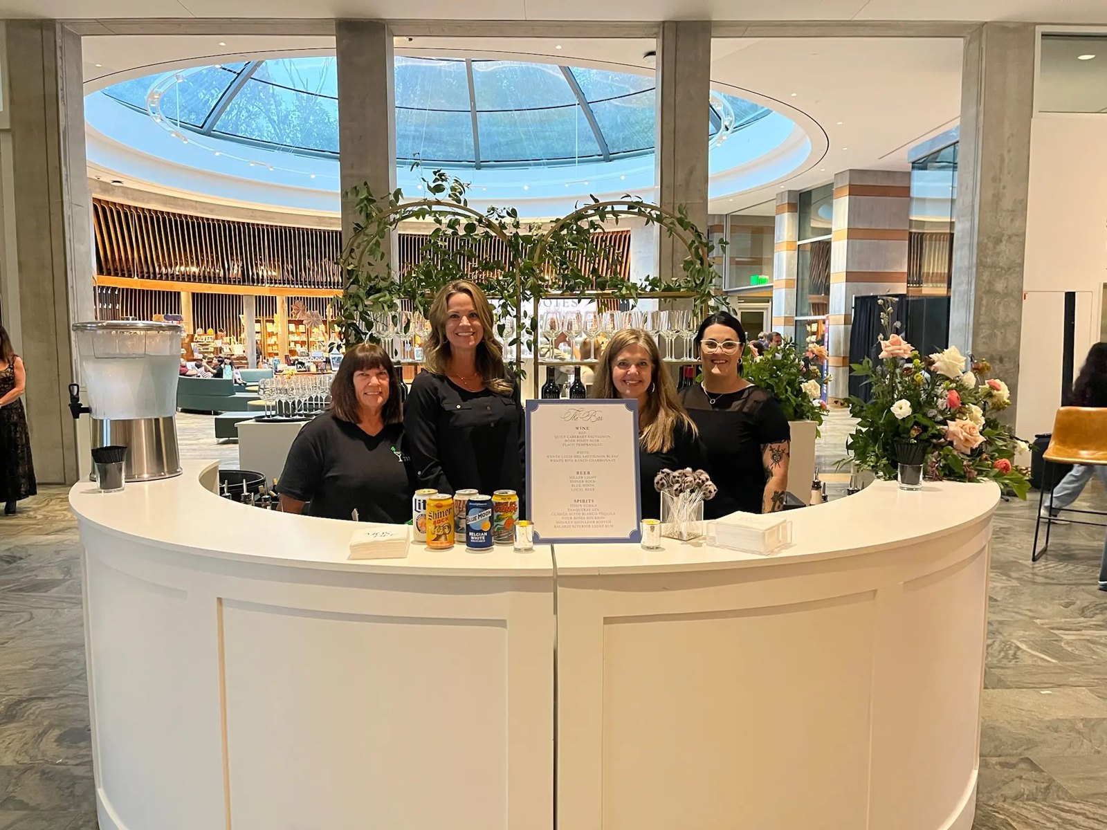 The Tie 1 On crew behind a round white bar under a glass dome
