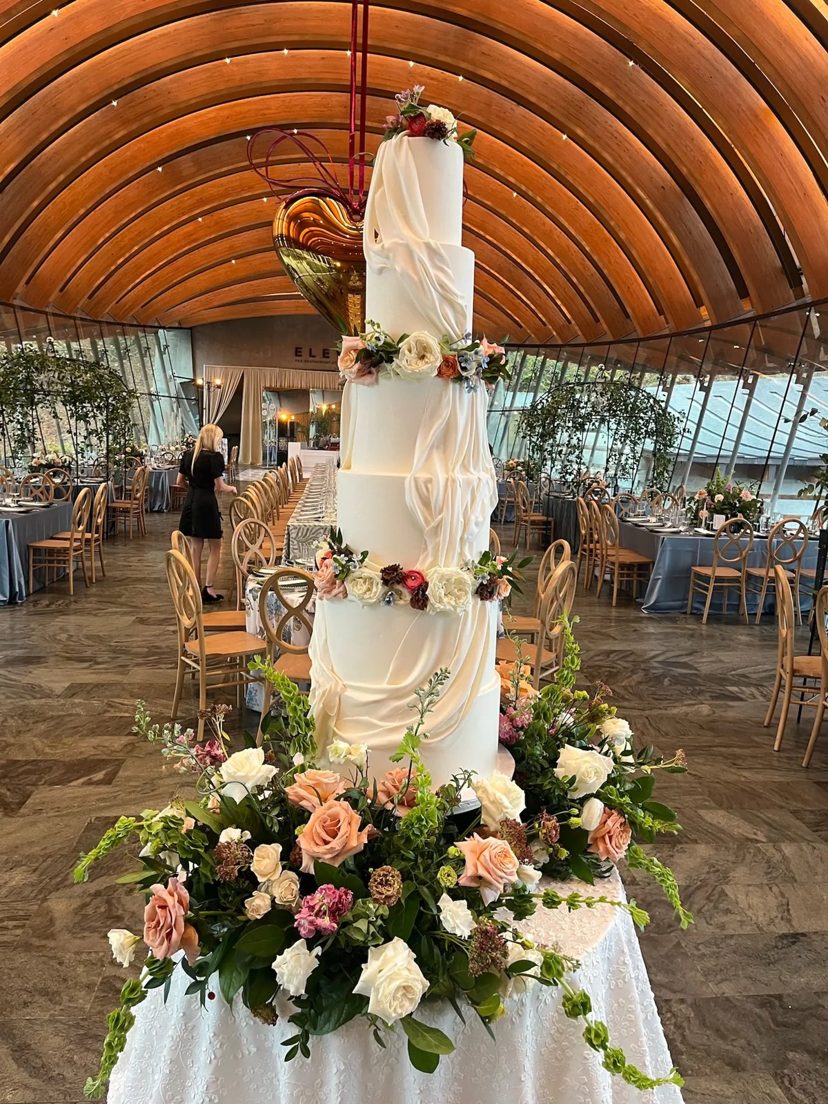 A tall white wedding cake with blush florals in a timber-vaulted venue