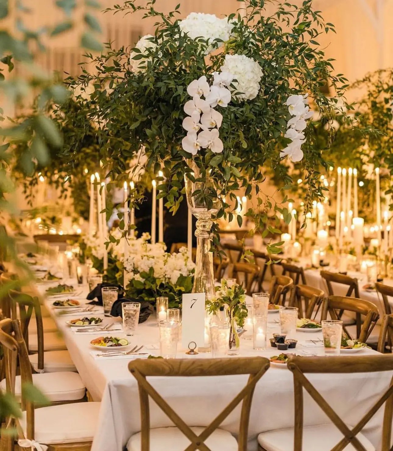 A candlelit wedding reception table beneath a tree of white orchids