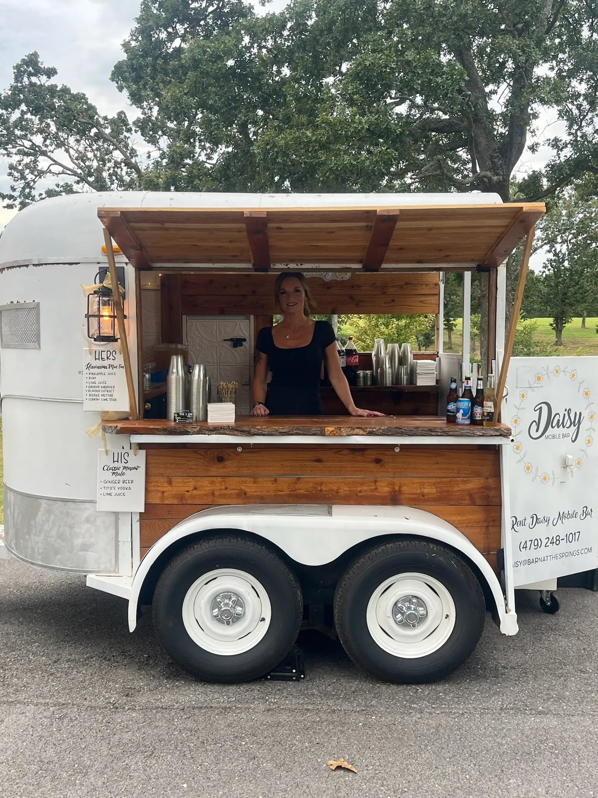 A bartender serving from a converted horse-trailer bar at an outdoor wedding
