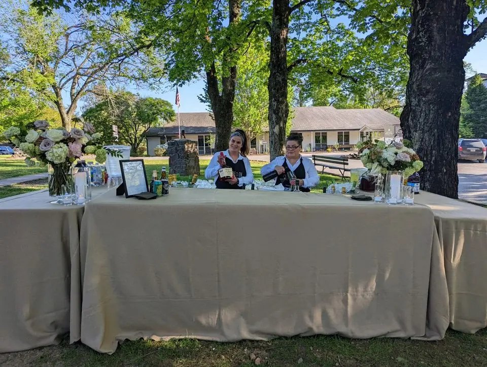 A linen-draped bar set up on a lawn under shade trees
