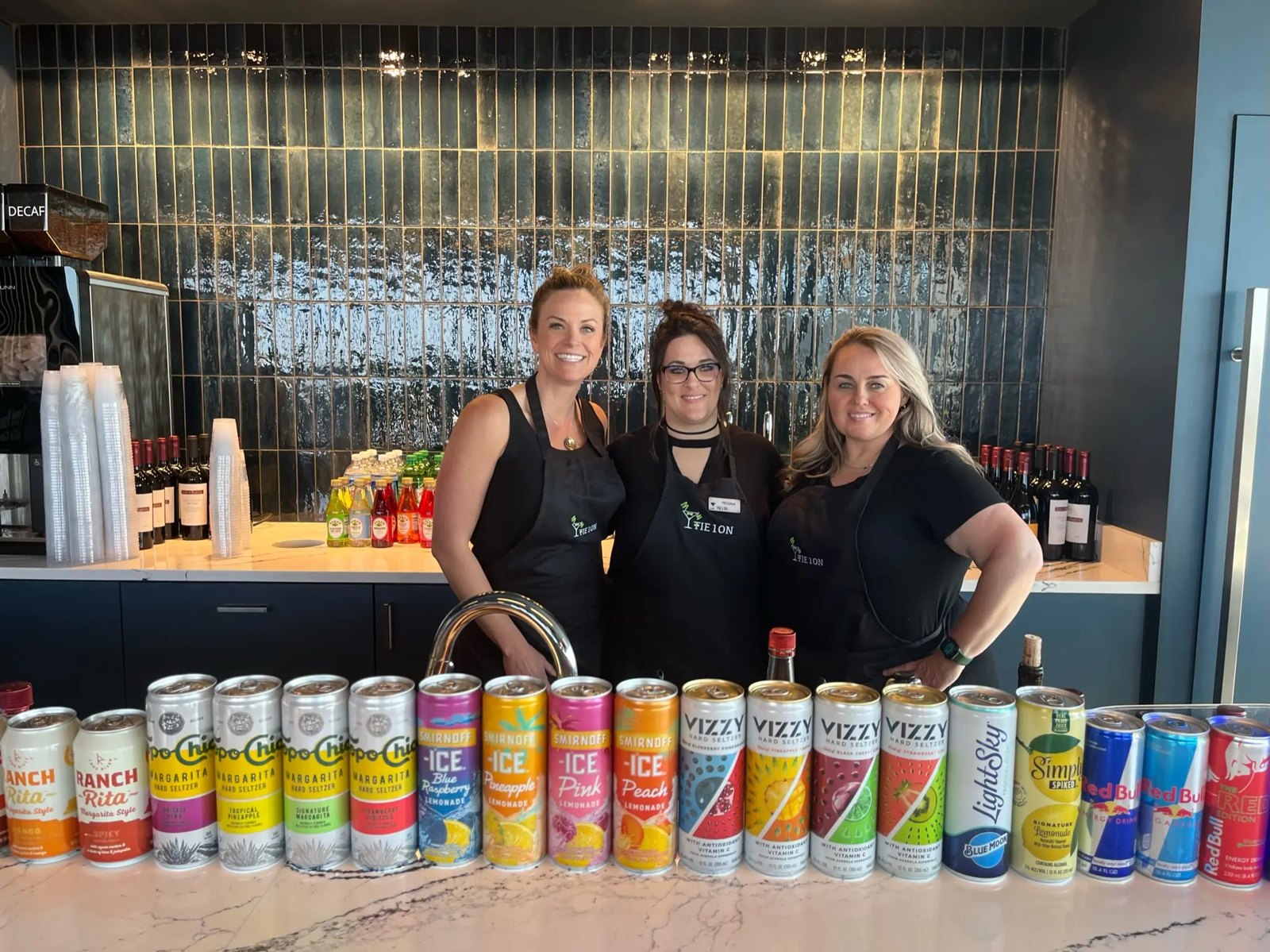 Three Tie 1 On bartenders behind a home bar stocked with canned cocktails